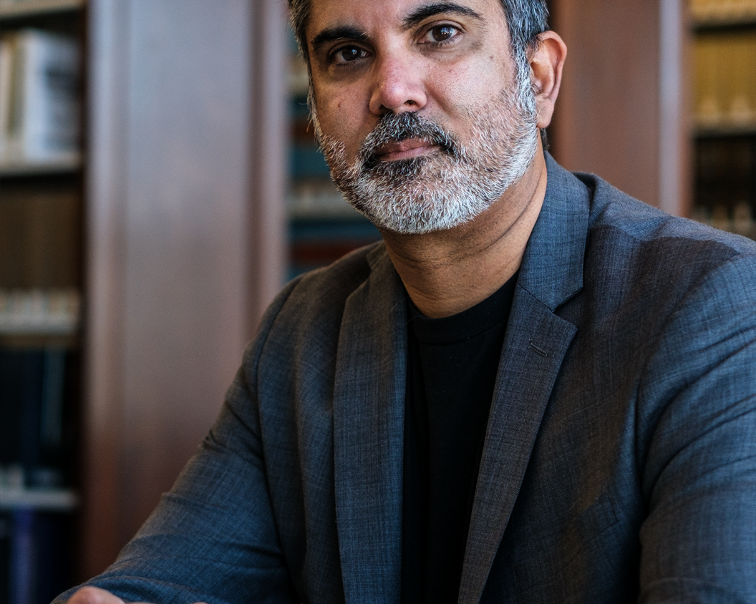 Photograph of a male member of faculty pictured in a library wearing a dark suit.