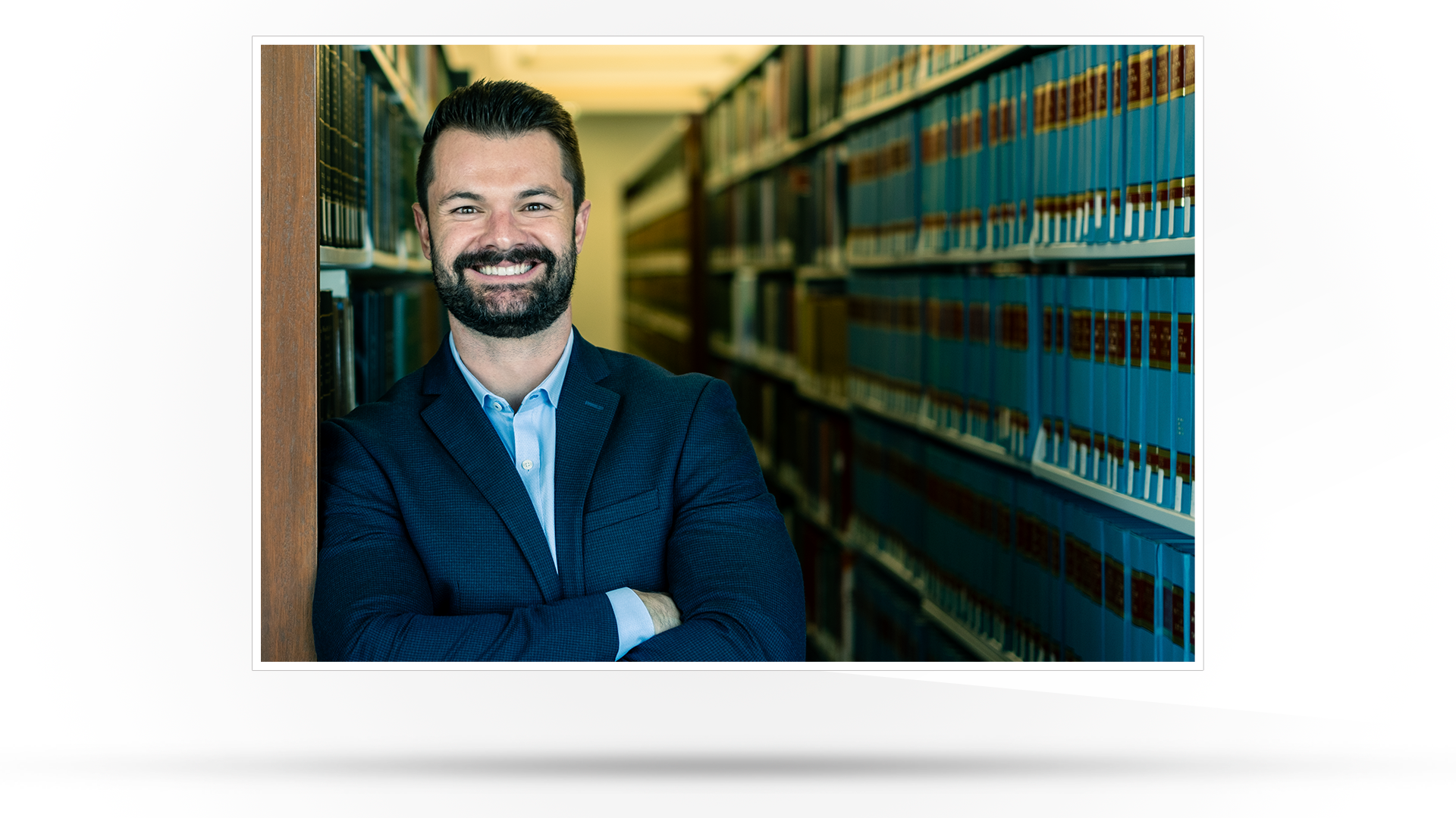 Copywriting Interview Profile picture: Photograph of a smiling man pictured in a library wearing a dark suit.
